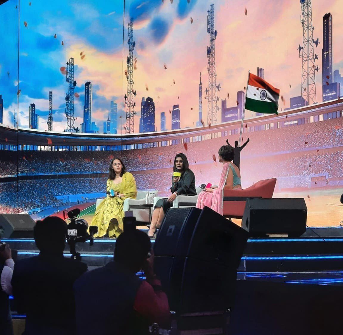 Saina Nehwal on a panel discussion stage with a stadium backdrop
